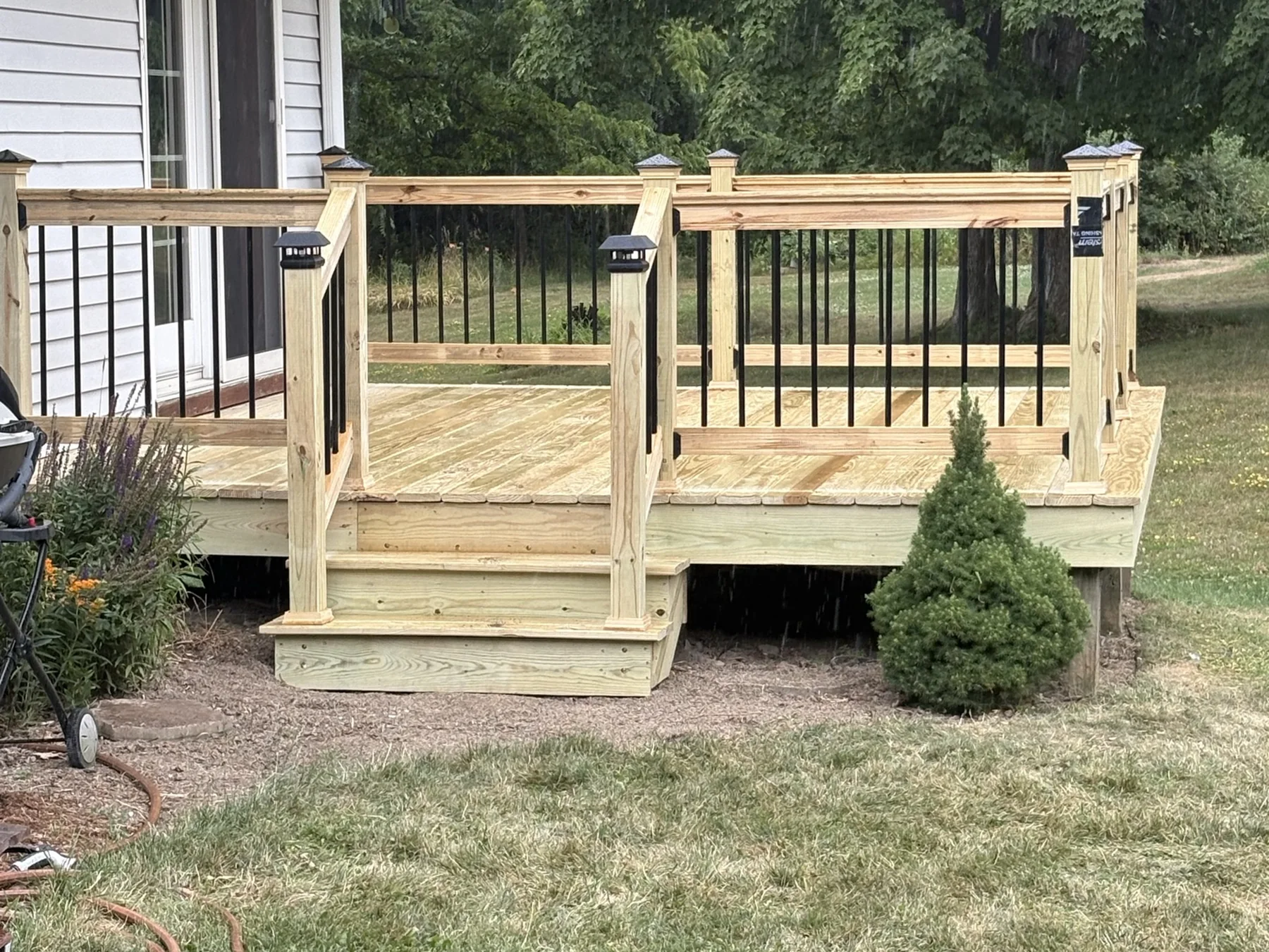 Finished farmhouse deck with black balusters and wide steps leading to the lawn.